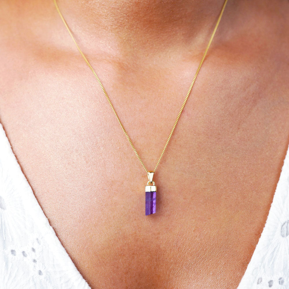  Halskette mit violetter Amethystspitze. Goldene Halskette mit Amethyst-Edelstein mit goldenen Details, wie ein Amulett gegen negative Energien.